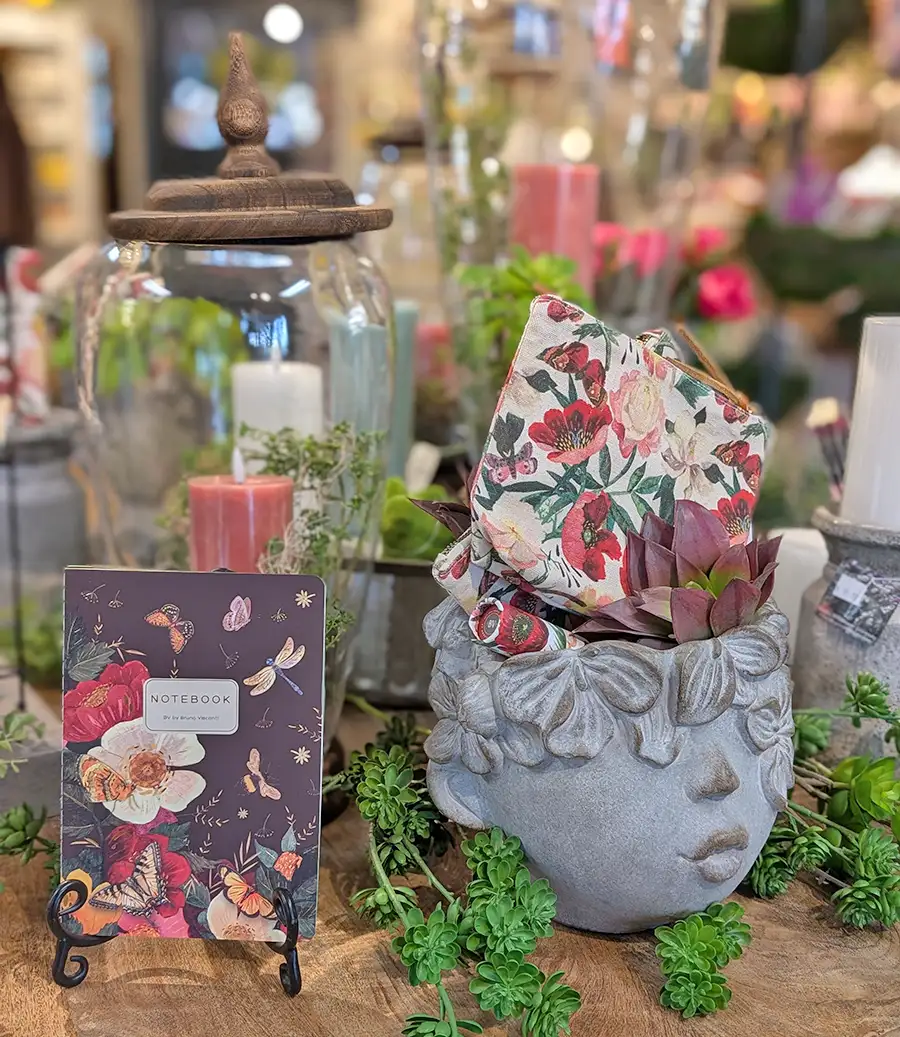 Summer home decor featuring faux plants, floral napkins, floral patterned notebook, and a head planter with a kissing face on it